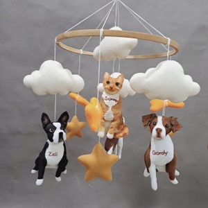 May include: A white, brown, and yellow baby mobile with a cat, two dogs, and clouds. The cat is named Sonny, one dog is named Gordy, and the other dog is named Zeli.