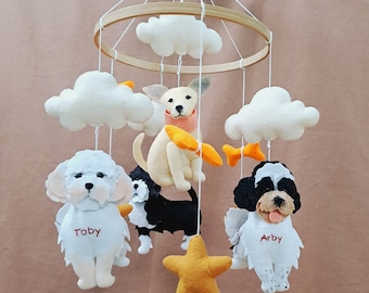 May include: A white felt baby mobile with a wooden ring, featuring four felt dog characters, two white clouds, and a yellow star. The dogs are named Toby, Arby, and two others.