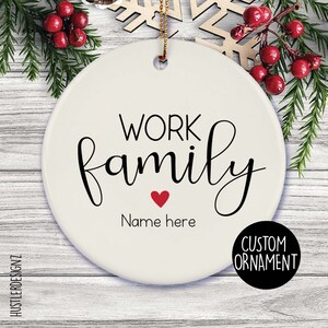 Peut inclure: Ornement personnalisé en céramique blanche avec les mots "WORK family" en écriture noire et un cœur rouge. Le texte "Name here" est en dessous du cœur. Un cercle noir avec "CUSTOM ORNAMENT" est en bas à droite.