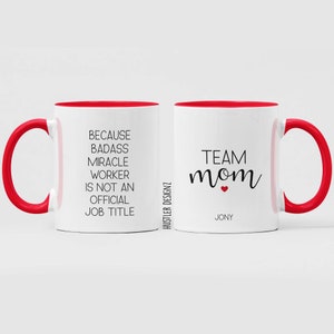 May include: White ceramic mug with a red rim and handle. The mug has black text that reads "Because Badass Miracle Worker Is Not An Official Job Title" on one side and "Team Mom" with a red heart on the other side. The text "Jony" is printed below the heart.