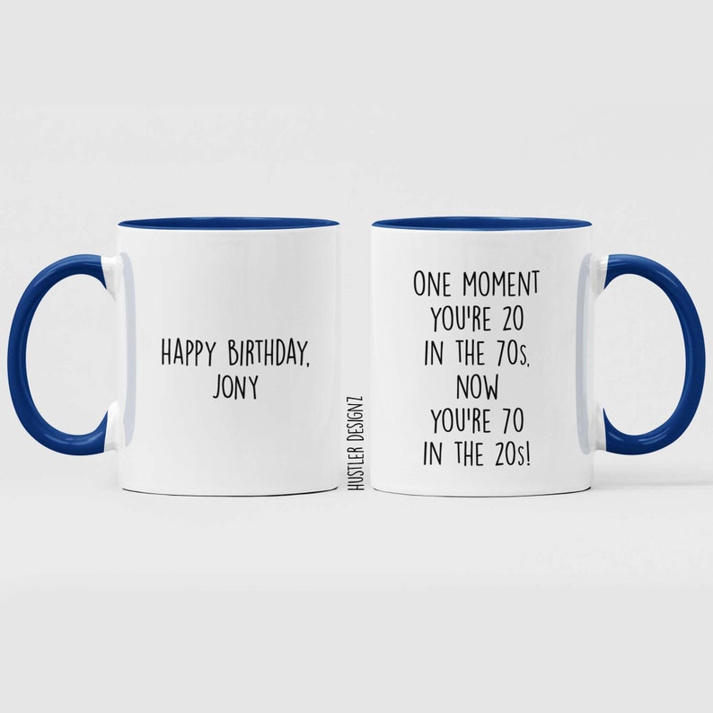 Może przedstawiać: Biały kubek ceramiczny z niebieskim rantem i uchwytem. Kubek ma napis "Happy Birthday, Jony" po jednej stronie i "One moment you're 20 in the 70s. Now you're 70 in the 20s!" po drugiej.