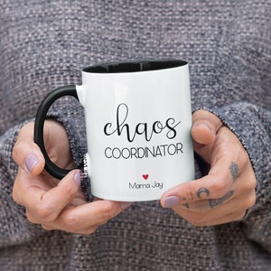 May include: White ceramic mug with a black handle and black rim. The mug has the text "chaos coordinator" and "Mama Jay" with a red heart in between.