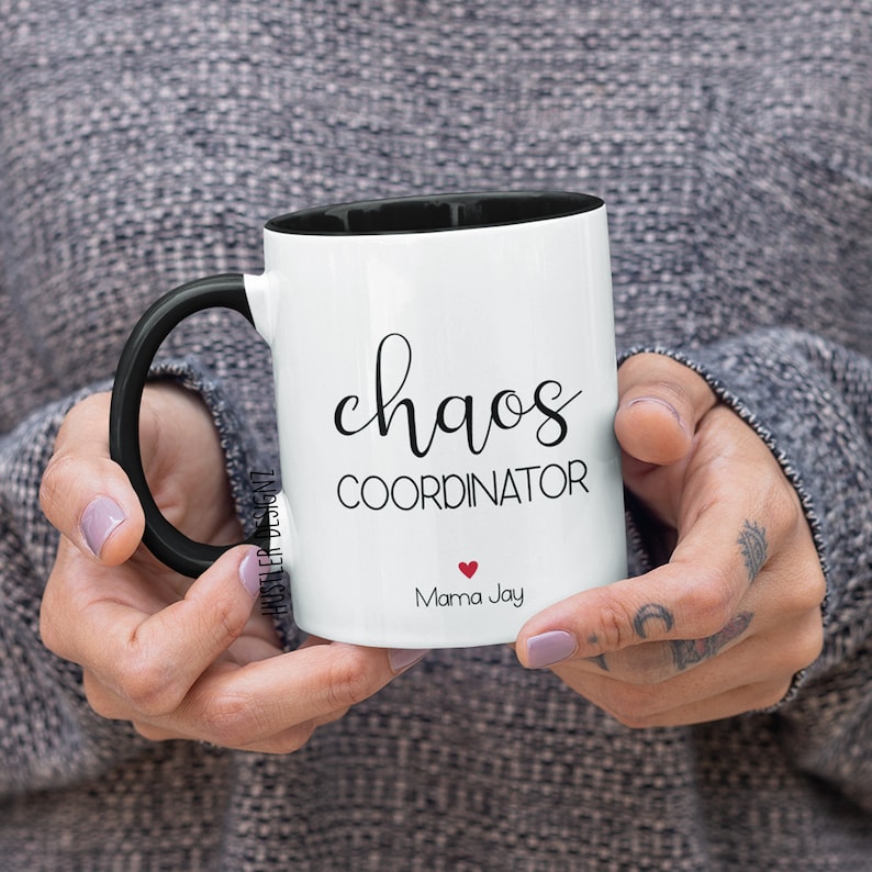 May include: White ceramic mug with a black handle and black rim. The mug has the text "chaos coordinator" and "Mama Jay" with a red heart in between.