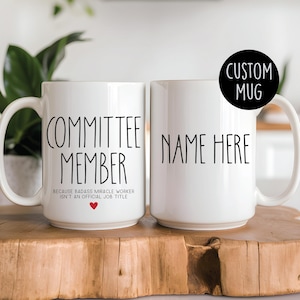 May include: Two white ceramic mugs with black text. The mug on the left says "Committee Member" and "Because badass miracle worker isn't an official job title." The mug on the right says "Name Here".