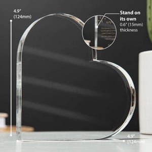 Puede incluir: Un marco de fotos de acr&iacute;lico transparente en forma de coraz&oacute;n, de 12,4 cm de alto y 1,5 cm de grosor. Se sostiene por s&iacute; solo.