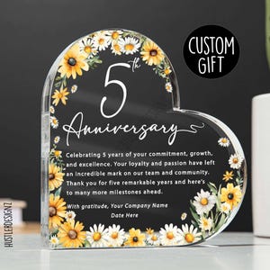 Könnte beinhalten: Ein herzförmiges, transparentes Acryl-Geschenk mit schwarzem Hintergrund. Der Text lautet "5. Jahrestag" mit einem Blumendesign aus gelben und weißen Gänseblümchen. Der Text "Custom Gift" befindet sich in einem schwarzen Kreis.