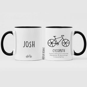 May include: Two white ceramic mugs with black handles and black rims. The mug on the left has the name "JOSH" printed on it and a small bicycle illustration. The mug on the right has a larger bicycle illustration and the word "CYCOPATH" printed below it. The definition of "CYCOPATH" is printed below the word: "A person suffering from chronic bike riding disorder with abnormal urges to ride and feel free."