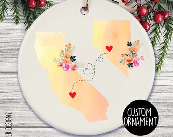 Puede incluir: Adorno de cerámica blanca con ilustraciones de acuarela de California y Nevada, conectadas por una línea punteada con corazones. Cada estado tiene un arreglo floral. El adorno tiene el texto "CUSTOM ORNAMENT".