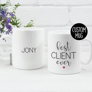 Könnte beinhalten: Zwei weiße Keramikbecher. Ein Becher hat den Namen "Jony" darauf gedruckt. Der andere Becher hat den Text "best CLIENT ever" darauf gedruckt mit einem kleinen roten Herzen.