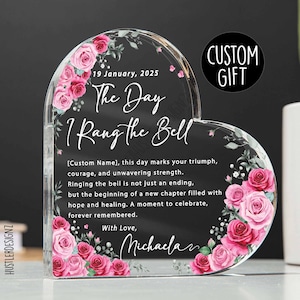 May include: A heart-shaped acrylic custom gift with floral detailing and the inscription "The Day I Rang the Bell." The design includes the date 19 January, 2025, and a personalized message. A "Custom Gift" sticker is also visible.