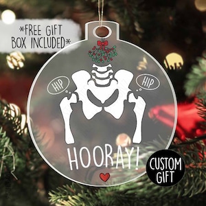 May include: Clear, round Christmas ornament with a skeleton hip bone design. The ornament has the word "HOORAY!" and a red heart at the bottom. The words "HIP" are in speech bubbles. The ornament also has a mistletoe design and the words "CUSTOM GIFT".
