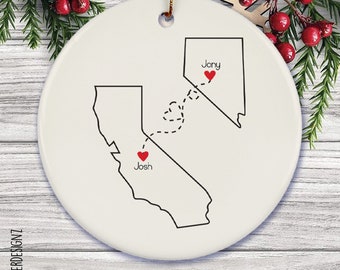 Puede incluir: Adorno navideño de cerámica blanca con los contornos de California y Nevada. Las ubicaciones de "Josh" y "Jony" están marcadas con corazones rojos, conectados por una línea de puntos. El adorno tiene una cuerda dorada para colgar.