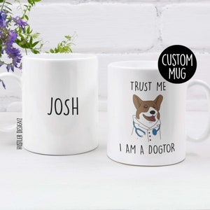 May include: White ceramic mug with the name "Josh" printed on one side and a cartoon corgi wearing a doctor's coat and stethoscope on the other side. The text "Trust me I am a Dogtor" is printed below the corgi. The mug is labeled "Custom Mug".