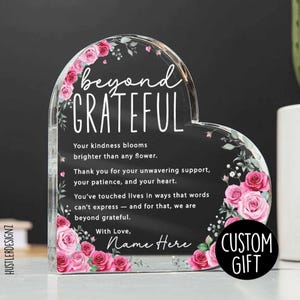 May include: Heart-shaped acrylic gift with the words "beyond GRATEFUL" in white script. Pink roses and green leaves decorate the edges. The text includes a personalized message and the words "CUSTOM GIFT".