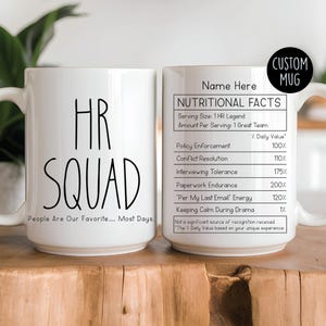 Op de afbeelding: Witte keramische mok met de tekst "HR SQUAD" in zwart, evenals "People Are Our Favorite... Most Days." De mok heeft ook een "Nutritional Facts" label met humoristische HR-gerelateerde statistieken. Een "Custom Mug" label is ook zichtbaar.