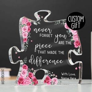 Puede incluir: Pieza de rompecabezas de acrílico transparente con rosas rosas y el texto "never forget you are the piece that made the difference." Incluye una pegatina "Custom Gift" y espacio para un nombre.