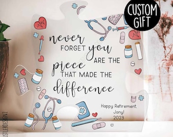 May include: A white acrylic puzzle piece with a medical theme. The puzzle piece has a blue and white stethoscope, pills, bandages, and a thermometer. The text on the puzzle piece reads "Never forget you are the piece that made the difference." The text "Happy Retirement. Jony! 2023" is also on the puzzle piece.