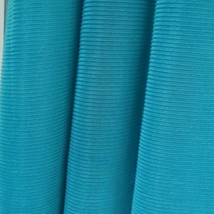 May include: Close-up of a teal blue fabric with a ribbed texture. The fabric is folded in a way that shows the texture and the colour.