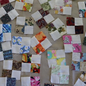 Puede incluir: Una colección de cuadrados de tela para acolchado. Cada cuadrado presenta una esquina blanca y una esquina estampada con diseños florales, geométricos y abstractos en varios colores. Ideal para proyectos de costura.