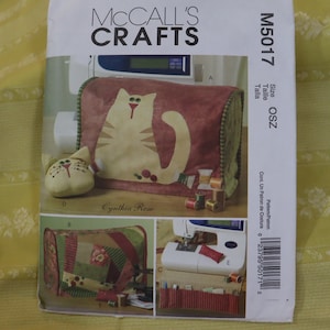 May include: A McCall's Crafts sewing pattern featuring a cat design. The pattern includes images of a sewing machine cover, a cat-shaped pin cushion, and other sewing accessories. The pattern is labeled M5017.