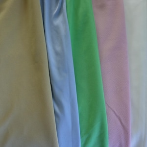 May include: A close-up of several fabric swatches in various colors. The colors include beige, light blue, green, light pink, and white. The fabric appears to be soft and flowing, with subtle textures visible.