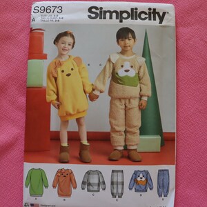 Può includere: Modello di cucito Simplicity per bambini a tema animali. Il modello presenta un vestito da orso giallo e un pigiama a tema cane beige. Il modello include taglie IT 3-8. Il logo Simplicity è in alto.