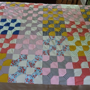 May include: A patchwork quilt with a variety of colors and patterns, including pink, yellow, blue, red, and white. The quilt is made up of squares with a geometric design.