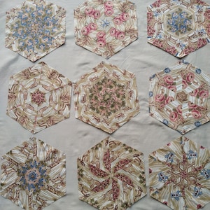 Puede incluir: Nueve bloques hexagonales de patchwork de tela con una variedad de patrones florales y geométricos en tonos marrones, rosas, azules y verdes. Los bloques están dispuestos en tres filas de tres.