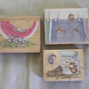 Może przedstawiać: Trzy drewniane stemple z fantazyjnymi ilustracjami. Jeden przedstawia myszy z kawałkiem arbuza, drugi myszy w dżinsowych ogrodniczkach, a ostatni myszy z workiem ziaren kawy.
