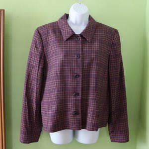 May include: A burgundy plaid blazer with a collared neckline and button-down closure. The blazer features a classic plaid pattern in shades of burgundy, brown, and a hint of blue. The jacket is displayed on a white mannequin.