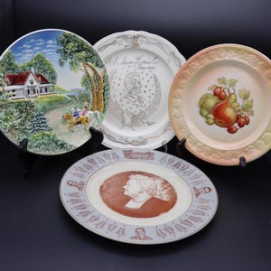 May include: Four decorative plates with various designs. One plate features a landscape with a house and figures on horseback. Another plate has a portrait of Abraham Lincoln. A third plate displays pears and berries. The fourth plate has a portrait of a woman.