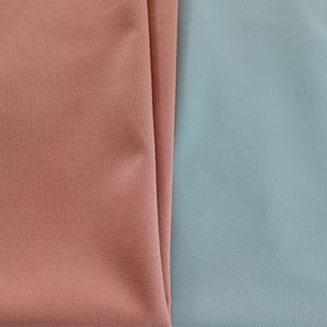 May include: Close-up of two fabric swatches. One is a muted coral color, and the other is a soft, dusty blue. The fabrics are folded, showing their texture and color variations. The image highlights the contrast between the two colors.