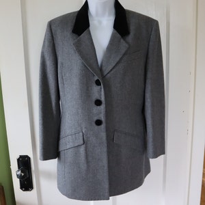 May include: A gray blazer with a black velvet collar and three black buttons. The blazer has two front pockets and is displayed on a mannequin. The blazer is a classic style.