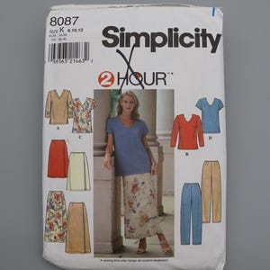 May include: A Simplicity sewing pattern packet, featuring illustrations of various tops, skirts, and pants. The packet includes a photo of a woman wearing a blue top and floral skirt. The pattern number is 8087.