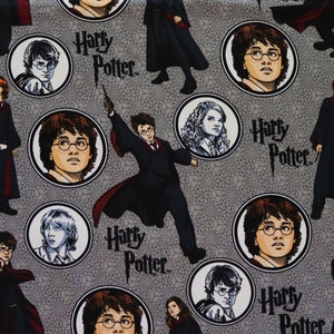 Op de afbeelding: Grijze stof met een herhaald patroon van Harry Potter-personages en het serielogo. Het ontwerp bevat portretten van Harry, Ron en Hermelien in cirkelvormige kaders, samen met actieposes van Harry met zijn toverstaf.
