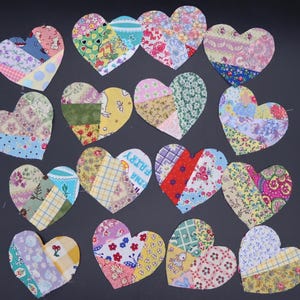 May include: A collection of colorful, patchwork fabric hearts in various sizes and patterns. Each heart is composed of different fabric pieces, featuring floral, striped, and dotted designs. The hearts are arranged on a dark gray surface.