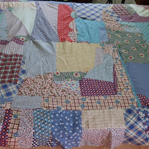 May include: A patchwork quilt made from various fabrics in shades of blue, green, red, and yellow. The quilt is made up of squares and rectangles of different sizes and patterns.