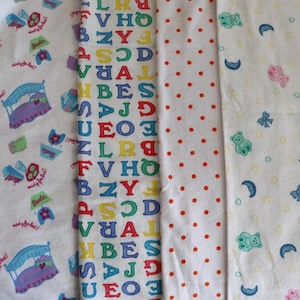 May include: A collection of white fabric swatches with various patterns. One features colorful letters, another has red polka dots, and others display repeating designs of beds, dresses, and toys. The fabrics are likely for children's items.