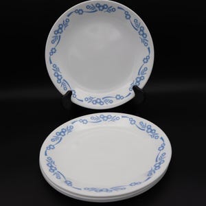 May include: White ceramic plates with a blue floral design around the rim. The plates are stacked and displayed against a black background. The floral pattern is a repeating design of small flowers and leaves.