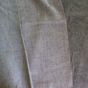 May include: Close-up of three sections of gray fabric. The left section is a solid, smooth weave. The center section has a herringbone pattern. The right section is a textured, solid weave. The fabrics appear to be wool or a wool blend.