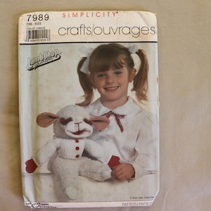 May include: Simplicity sewing pattern for a Lamb Chop puppet. The pattern cover features a young girl holding the puppet. The puppet is white with red accents. The pattern is labeled "7989" and "ONE SIZE".