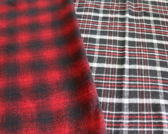 May include: Two pieces of fabric with plaid patterns. One is predominantly red and black, the other is black, white, and red. The fabrics are likely for apparel or home decor.