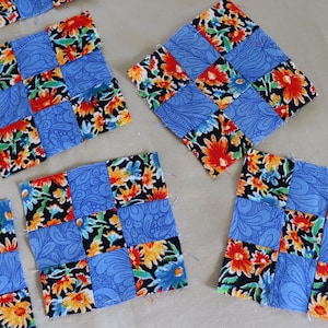 Może przedstawiać: Dziewięć kwadratów z tkaniny w kolorze niebieskim i białym z kwiatowymi wzorami, ułożonych w siatkę. Każdy kwadrat składa się z dziewięciu mniejszych kwadratów, tworząc efekt patchworku.