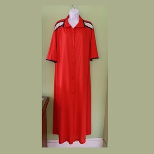 May include: A long, button-down, red robe with short sleeves. The robe has white and navy blue accents on the shoulders and collar. The robe is displayed on a white mannequin.