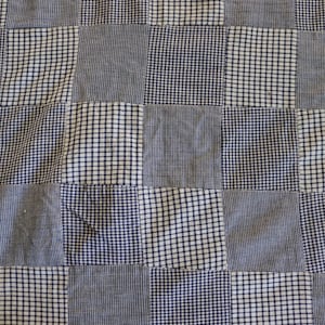 Puede incluir: Primer plano de un edredón de retazos con un patrón de cuadros. El edredón está compuesto por cuadrados alternos de telas blancas y azul marino. Las telas tienen varios patrones, incluyendo cuadros pequeños y colores lisos. El edredón parece hecho a mano.