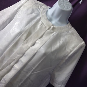 Puede incluir: Una blusa blanca de satén con estampado floral y cierre de botón en el cuello.