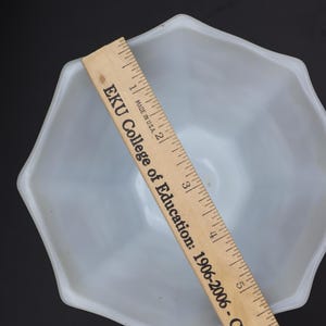 May include: A light blue, octagonal bowl with a wooden ruler laid across it. The ruler has text that reads "EKU College of Education: 1906-2006 - Celebrating O". The bowl is empty and sits against a black background.
