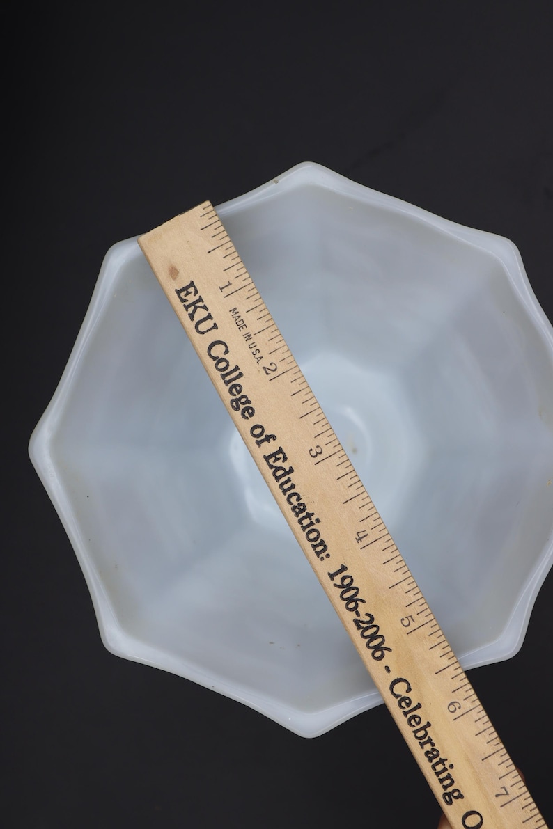May include: A light blue, octagonal bowl with a wooden ruler laid across it. The ruler has text that reads "EKU College of Education: 1906-2006 - Celebrating O". The bowl is empty and sits against a black background.