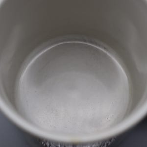 May include: A close-up shot of the inside of a white ceramic mug. The interior is smooth and slightly reflective, with a subtle gradient of light and shadow. The mug has a handle on the right side.