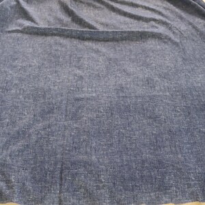 May include: A large expanse of blue fabric with a textured surface. The material is a solid colour with a slightly faded appearance, and it appears to be draped or folded. The fabric has a soft, flowing quality.